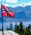 Norwegian flag waving on a wooden table with scenic fjord and mountain landscape in the background