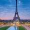 Eiffel Tower at dusk with city lights and cloudy sky.