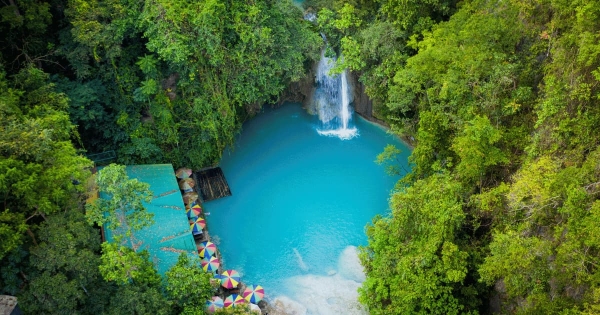 Aerial view of Kawasan Falls in Badian, Cebu, Philippines, showcasing turquoise blue waters, lush green rainforest, colorful umbrellas, and a serene tropical setting