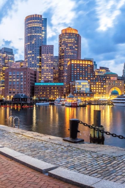 Boston Harbor waterfront at dusk with illuminated skyscrapers and boats in Massachusetts