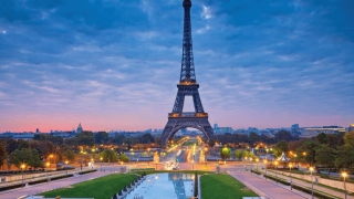 Eiffel Tower at dusk with city lights and cloudy sky.