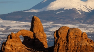 Turret Arch rock formation at Arches National Park, Utah, USA, with snow-capped La Sal Mountains in the background during winter.