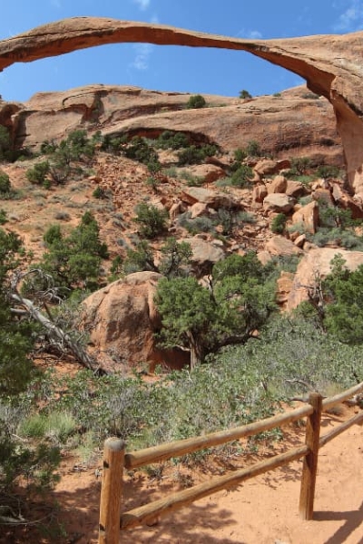 Scenic view of Landscape Arch along the hiking trail in Arches National Park, Utah, USA, surrounded by desert vegetation and red rock formations.