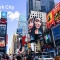 Times Square in New York City filled with colorful billboards, advertisements, and yellow taxis, with crowds of people walking on a bright day.