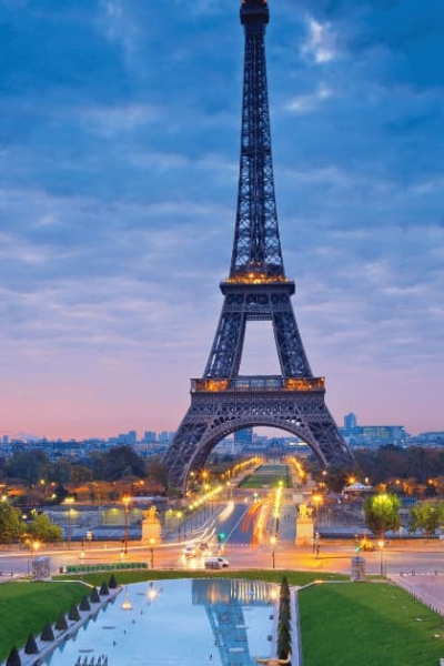 Eiffel Tower at dusk with city lights and cloudy sky.