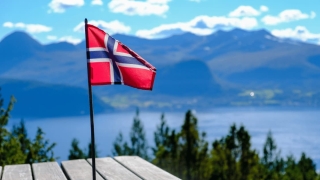 Norwegian flag waving on a wooden table with scenic fjord and mountain landscape in the background