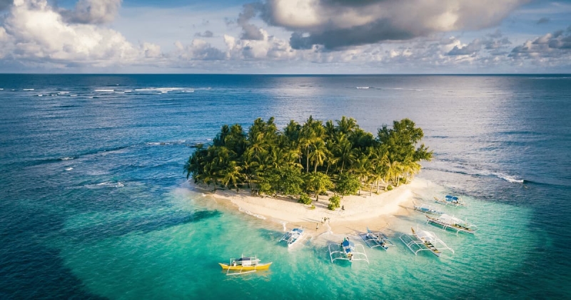 Stunning aerial shot of Guyam Island surrounded by turquoise waters, with palm trees and boats anchored along the beach in Siargao, Philippines