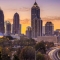 Atlanta skyline at sunset with tall skyscrapers and a curving highway lit by car lights in the foreground.