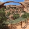 Scenic view of Landscape Arch along the hiking trail in Arches National Park, Utah, USA, surrounded by desert vegetation and red rock formations.