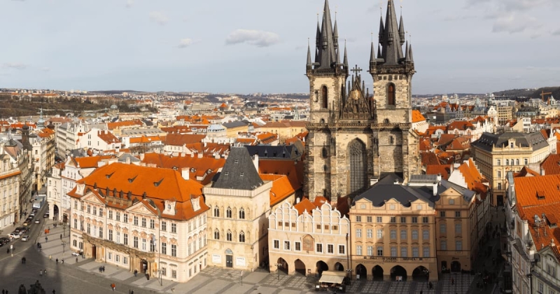 The towering Gothic spires of the Church of Our Lady before Týn overlook the historic Old Town Square in Prague, Czechia, surrounded by colorful baroque buildings with red tile roofs