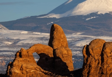 Turret Arch rock formation at Arches National Park, Utah, USA, with snow-capped La Sal Mountains in the background during winter.