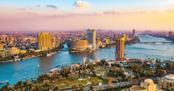 Panoramic view of Cairo, Egypt with the Nile River, modern skyscrapers, bridges, and lush green spaces at sunset.