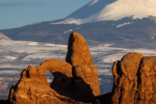 Turret Arch rock formation at Arches National Park, Utah, USA, with snow-capped La Sal Mountains in the background during winter.