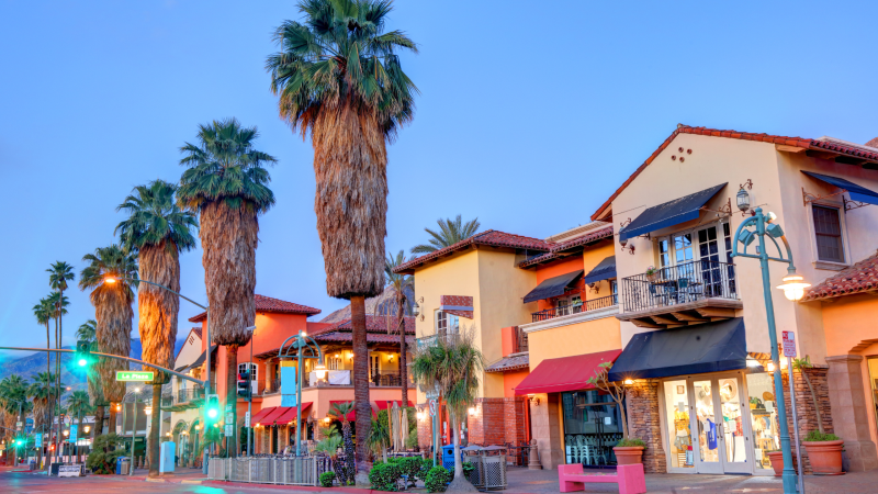 Colorful Spanish-style buildings and tall palm trees along Palm Canyon Drive in Palm Springs, California, at sunset.