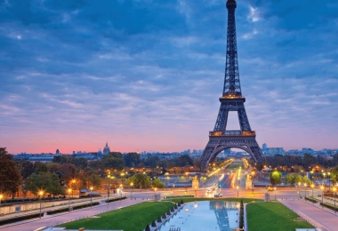 Eiffel Tower at dusk with city lights and cloudy sky.