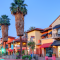 Colorful Spanish-style buildings and tall palm trees along Palm Canyon Drive in Palm Springs, California, at sunset.