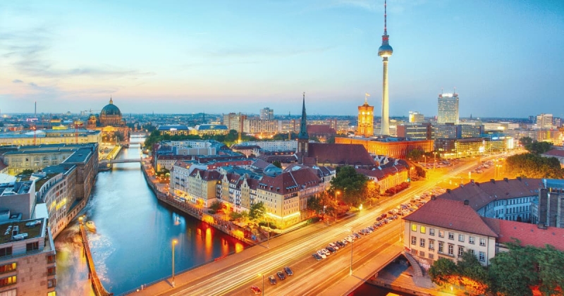 The vibrant heart of Berlin, Germany, glows as twilight settles, showing the Spree river winding past historic buildings and the iconic Fernsehturm television tower dominating the evening sky