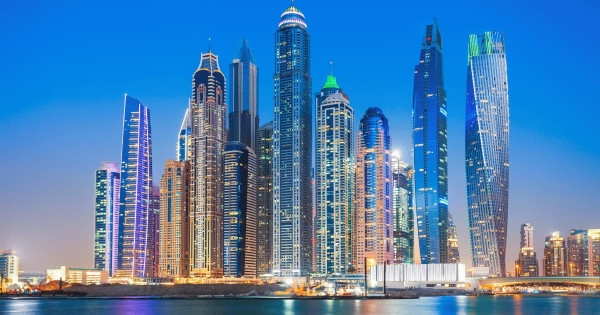 Dubai Marina skyline at dusk with illuminated skyscrapers reflecting on the waterfront.