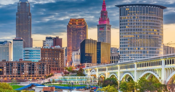 Downtown Cleveland skyline at sunset with illuminated skyscrapers and the Hope Memorial Bridge in the foreground.