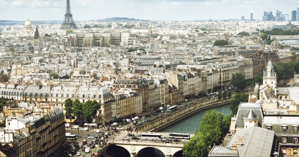 A panoramic view of Paris featuring the Eiffel Tower in the background, historic Haussmann-style buildings, and the Seine River flowing through the city.