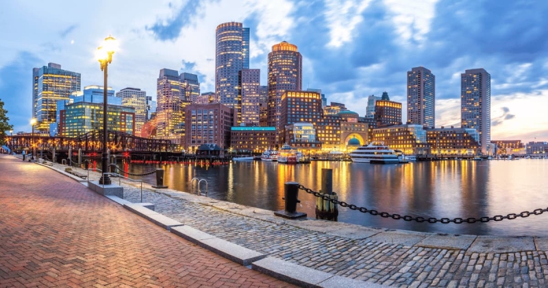 Boston Harbor waterfront at dusk with illuminated skyscrapers and boats in Massachusetts