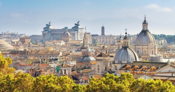 Panoramic view of Rome, Italy with historic domes, rooftops, and the Altare della Patria monument under a clear sky.