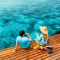 Romantic couple enjoying drinks on an overwater deck at a tropical island resort, overlooking the crystal-clear blue ocean in the Maldives.