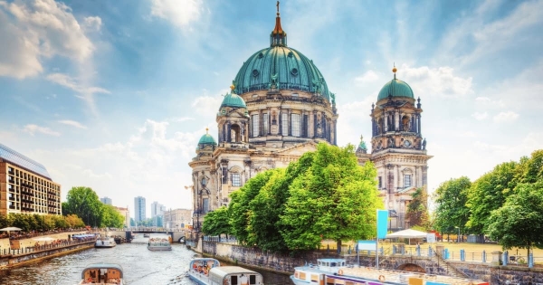 A summer day on the Spree river in Berlin, Germany, with river cruise boats passing by the magnificent green dome of the Berlin Cathedral under a bright blue sky