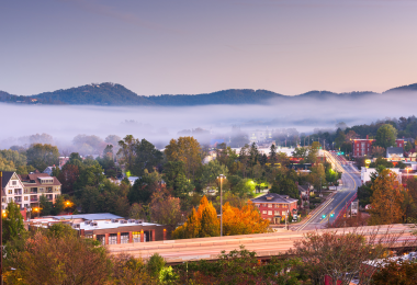 Scenic view of Asheville, North Carolina, with fog rolling over the Blue Ridge Mountains and fall foliage surrounding the city streets.