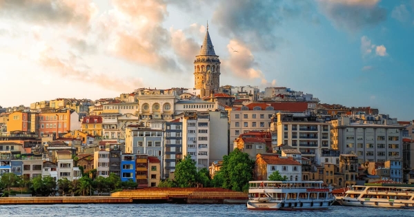View of Galata Tower and colorful buildings in Istanbul, Turkey with boats on the Bosphorus at sunset.