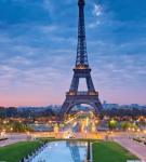 Eiffel Tower at dusk with city lights and cloudy sky.