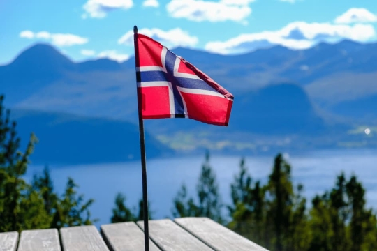 Norwegian flag waving on a wooden table with scenic fjord and mountain landscape in the background